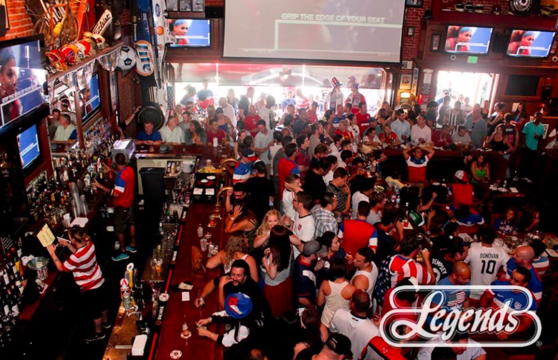 This image depicts the excited patrons enjoying a championship sporting event on the large projection screen offered at Legends Sports Bar in Long Beach, CA